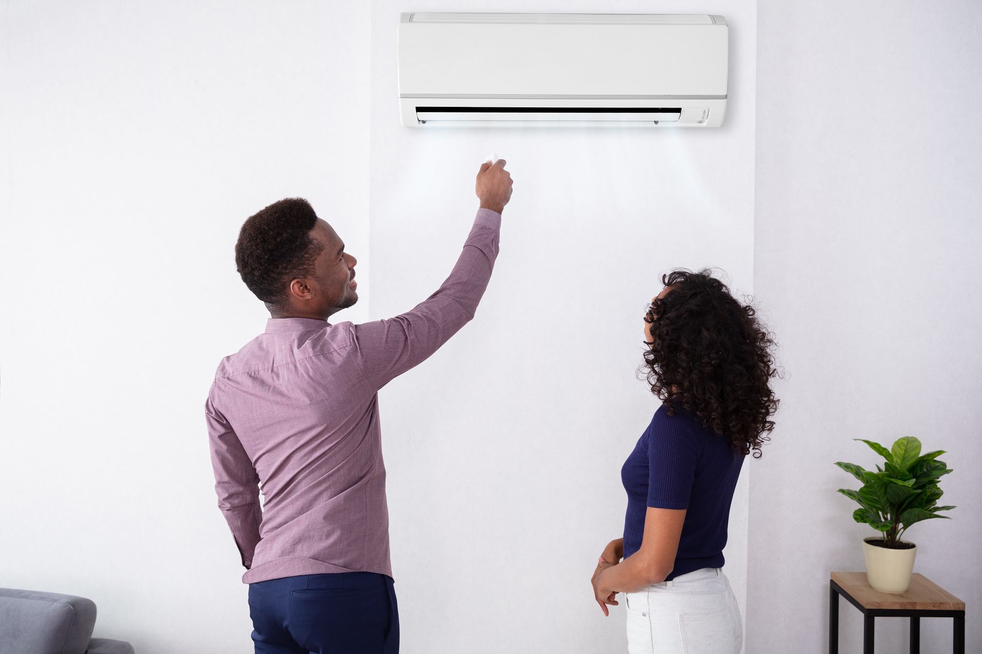 Couple Adjusting Temperature Of Air Conditioner
